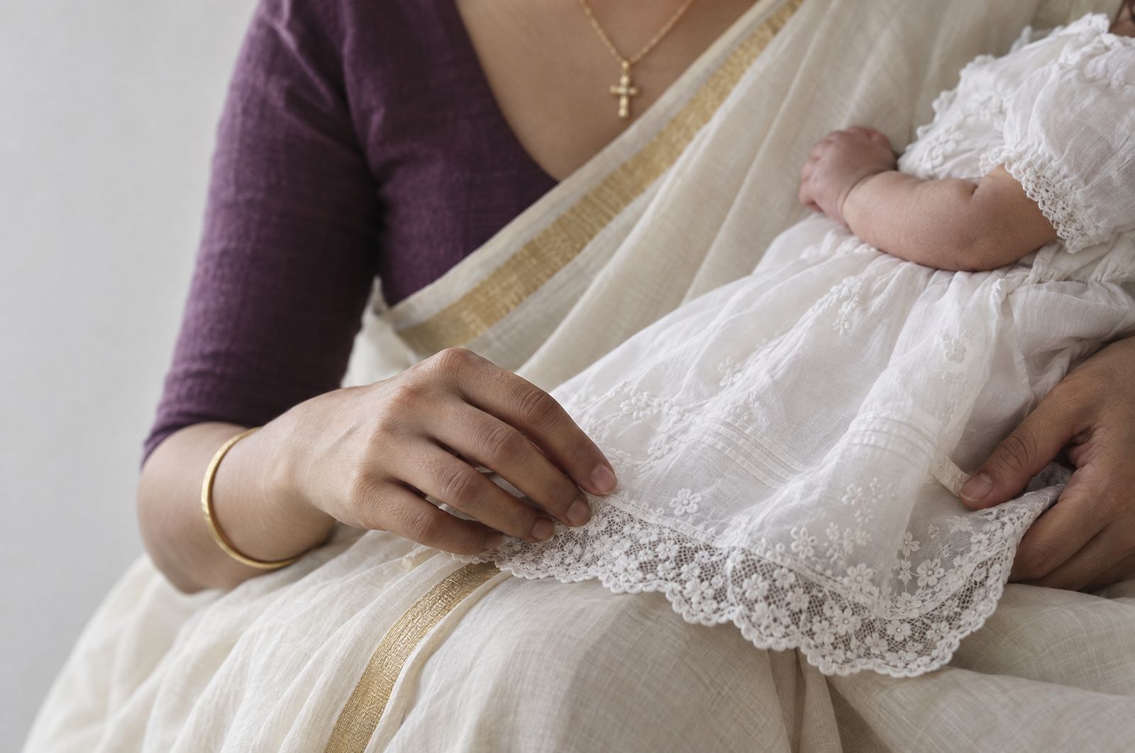A mother smooths the lace hem of a christening gown