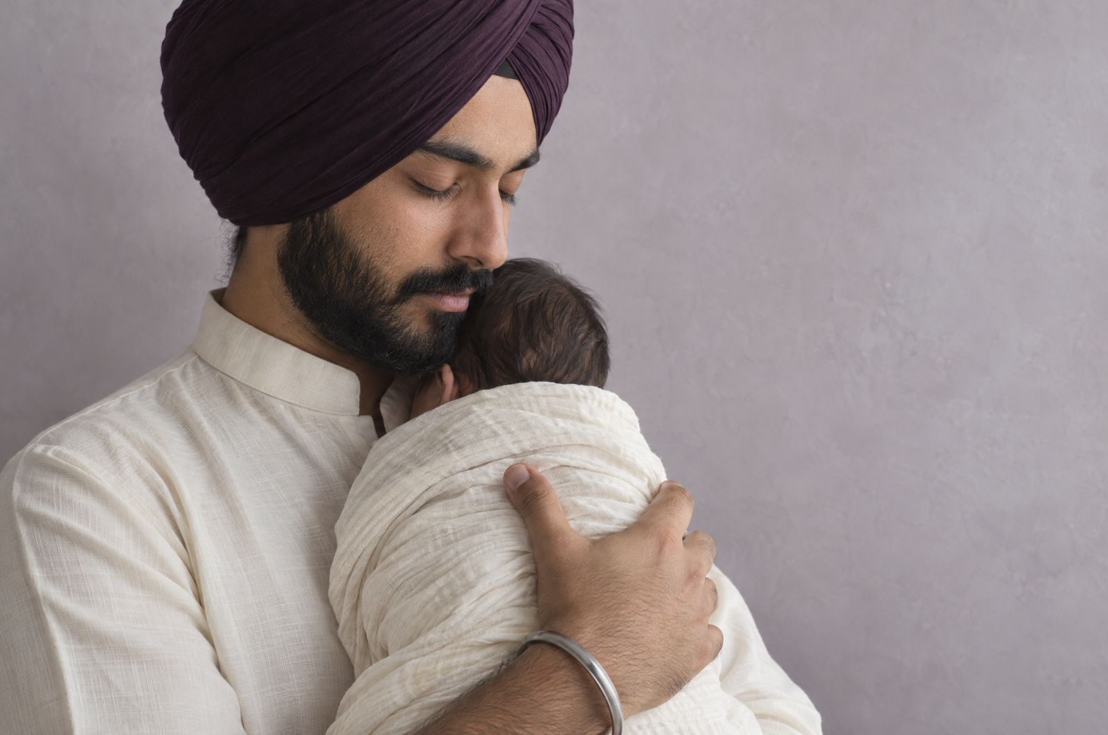 A Sikh father in a plum turban holds his newborn close